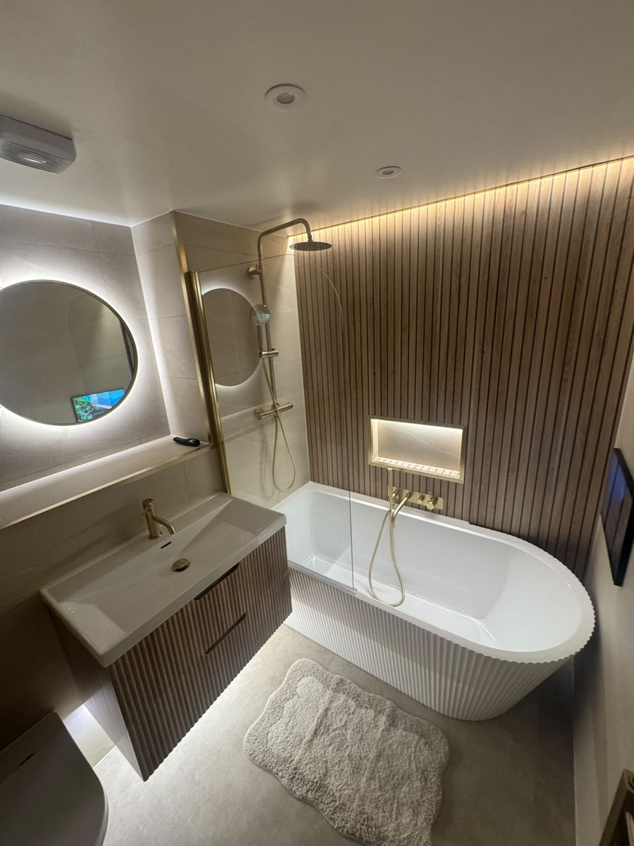 Round backlit mirror over fluted white bath with rainfall shower